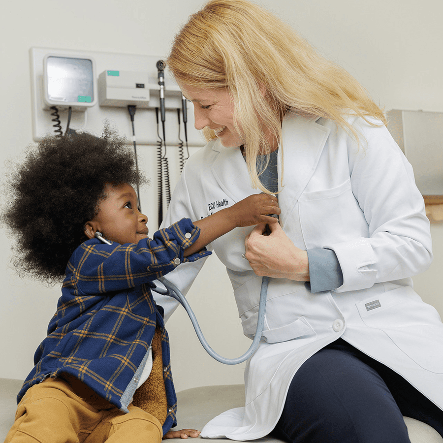 Smiling female doctor lets toddler listen to her heart through a stethoscope