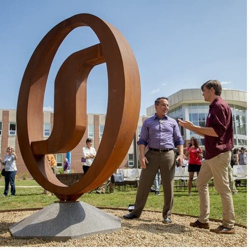 Todd Martin (right), a WCU fine arts student who produced the new “wi” sculpture on campus, discusses the work’s creation with Richard Sneed, principal chief of the Eastern Band of Cherokee Indians.