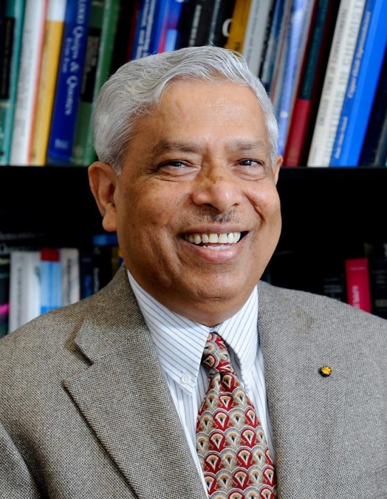 Dr. Narayan, smiling with a wall of books behind him
