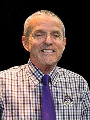 Carmen Russoniello smiling in a purple tie and ECU shirt