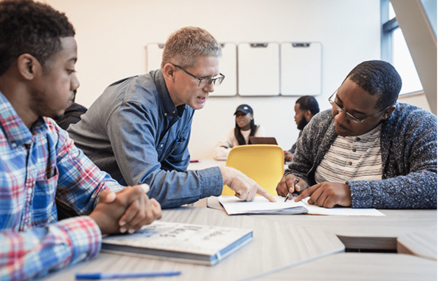 An advisor helps two male students complete forms.