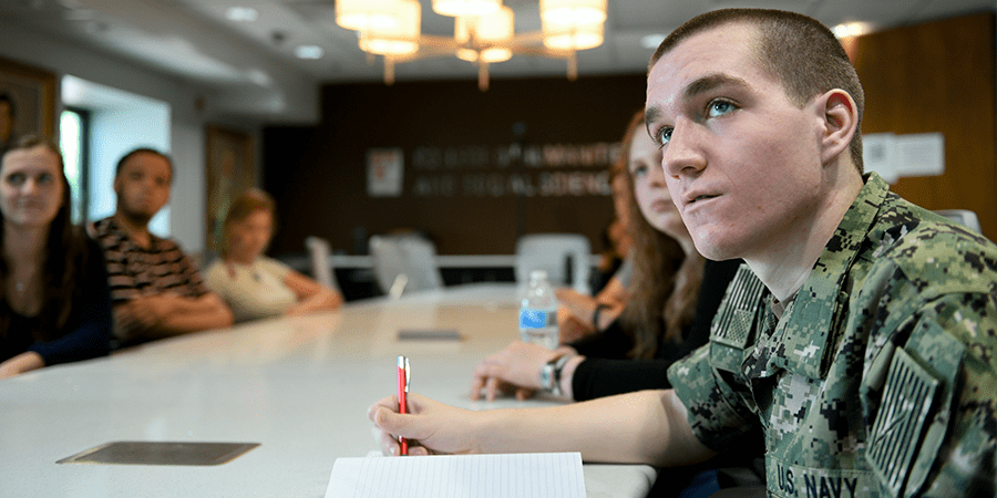 Student in a military uniform taking notes at a conference table